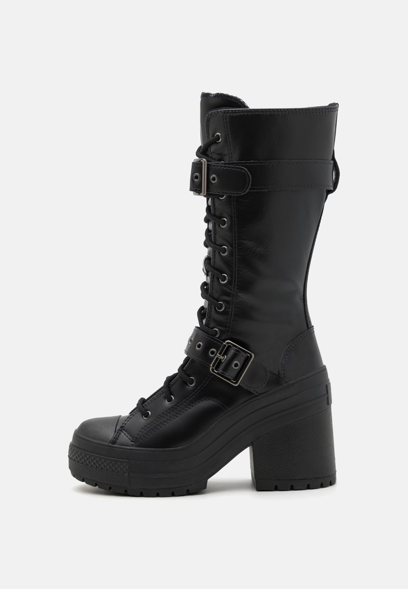 Bottes noires montantes en cuir avec un design à lacets, une sangle à boucle et un talon épais et massif pour plus de hauteur et de stabilité.