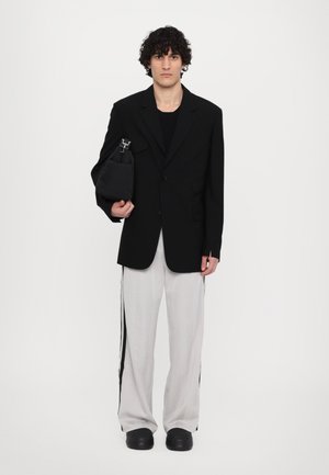 Svart oversized blazer over en svart topp, parret med lysegrå bukser med svarte sidestreker, og en liten svart skulderveske.