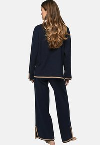 Ensemble lounge marine comprenant un haut à manches longues et un pantalon à jambes larges avec des finitions dorées aux poignets et à l'ourlet, confectionné dans un tissu doux et texturé.