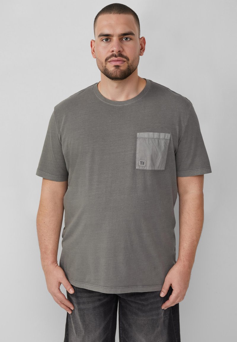 Szara koszulka z krótkim rękawem, z kieszonką na piersi w jaśniejszym szarym odcieniu. Tkanina wydaje się być miękka i lekko teksturowana.