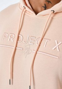 Licht perzikkleurige hoodie met een trekkoord, met geborduurde "PROJECT X" tekst en logo. Zachte stof met een gladde textuur en zilverkleurige hardware accenten.