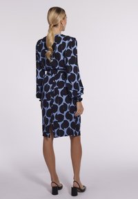 Czarna i niebieska sukienka z okrągłymi wzorami liści, z długimi rękawami, paskiem w talii i rozcięciem z boku. Gładki materiał o luźnym kroju.