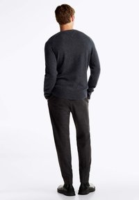 Maglione grigio lavorato a maglia con tessuto strutturato, polsini e orlo a costine, abbinato a pantaloni scuri a quadri e scarpe nere, visto da dietro.