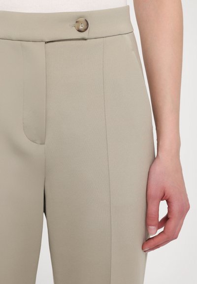 Bežīgas pielāgotas bikses ar gludu tekstūru, šauru piegriezumu, priekšējo kabatu un vienu dekoratīvu pogu jostasvietā.