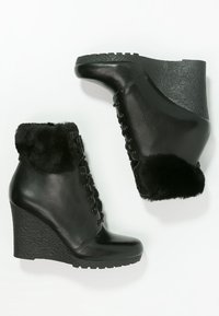 Bottines compensées noires avec poignets en fausse fourrure, devant à lacets, matériau en cuir lisse et semelles en caoutchouc texturé.