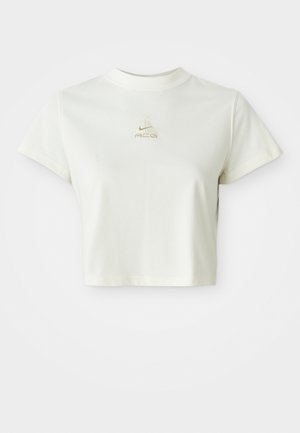 Trumpas baltas apkirptas marškinėliai su mažuoju smėlio spalvos Nike ACG logotipu, esančiu centre po apykakle.