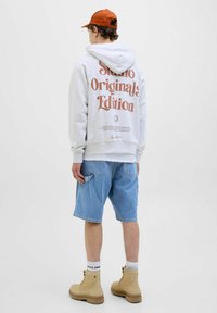 Grå hættetrøje med brun grafisk tekst, denim shorts, beige støvler og orange kasket. Afslappet outfit med en loose fit og bløde materialer.