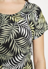 Černý top s krátkým rukávem se zeleným a bílým vzorem palmového listu. Má kulatý výstřih a žebrovanou texturu.
