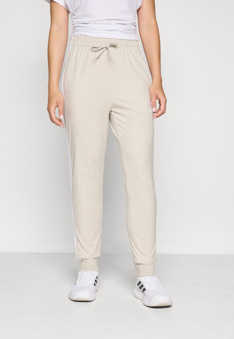 Bežové tepláky s elastickým pásom a nastaviteľným šnúrkou, s bielymi bočnými pruhmi a tesným manžetou na členkoch.