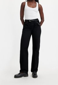 Black denim jeans with a high waist, wide-leg fit, and braided black belt. Paired with a white tank top and black chunky loafers.