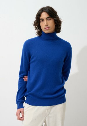 Blauwe coltrui gemaakt van zacht materiaal, met lange mouwen, een getailleerd ontwerp en geribde manchetten en zoom, gecombineerd met crèmekleurige corduroy broek.