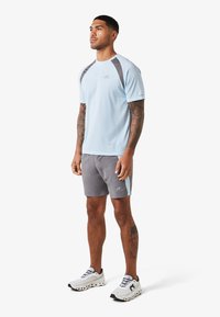 T-shirt de sport bleu clair avec des panneaux d'épaule gris contrastants, accompagné de shorts gris avec une accentuation bleu clair. Porté avec des baskets blanches.
