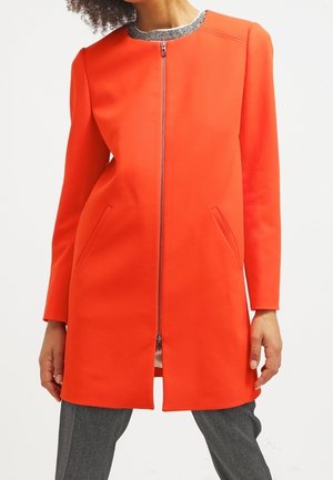 Manteau orange vif avec un col rond, fermeture éclair intégrale et poches latérales, doté d'un col texturé gris. Fini en tissu lisse.