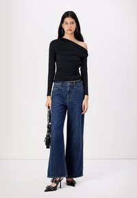 Haut noir à épaule unique, design ajusté, associé à un jean en denim sombre à jambes larges. Accessoirisé avec un sac noir et des chaussures à bout pointu.