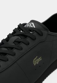 Black leather sneakers with flat laces, gold logo detail, textured surface, and quilted accents, featuring a classic low-top silhouette.