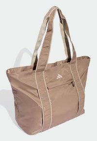 Saco tote em nylon bege com alças de tecido duplas, um bolso com fecho na frente e um pequeno logotipo. Apresenta uma textura brilhante e costuras reforçadas.