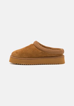 Brown suede slip-on shoe with a soft, rounded toe and padded collar. Features a textured rubber sole with a jagged edge. Minimal branding visible.