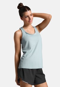 Canotta sportiva azzurro chiaro con scollatura rotonda, vestibilità slim e senza maniche, abbinata a pantaloni corti neri con una fessura laterale e dettagli bianchi.