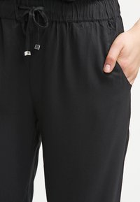 Pantalons de jogging noirs en tissu doux, dotés d'une taille élastique, d'un cordon de serrage et de poches latérales pour plus de praticité.