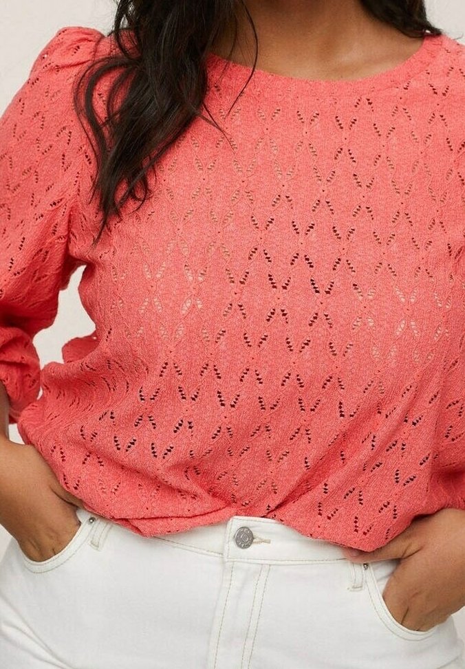 Top en coton corail à col rond, avec des manches bouffantes et un motif texturé ; porté sur un pantalon blanc taille haute.