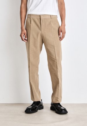 Beige tailored trousers made of soft fabric, featuring a flat front, side pockets, and a slim fit design, paired with black shoes.