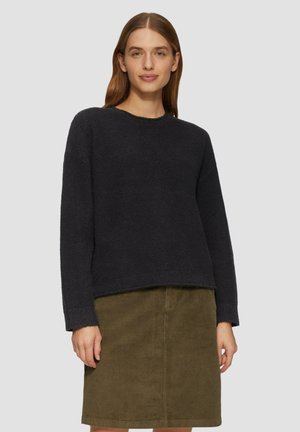 Dunkelgrauer gestrickter Pullover mit lockerer Passform und Rundhalsausschnitt, kombiniert mit einem cordelgrünen, strukturierten Midirock aus Cord. 