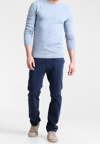 Light blue knit sweater with crew neck, paired with navy blue chinos and beige shoes. Simple design, smooth texture, and fitted silhouette.