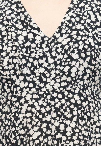 Μαύρο φόρεμα από ύφασμα με λευκό αφηρημένο μοτίβο λουλουδιών και βαθιά V-λαιμόκοψη, εμφανίζεται από το στήθος μέχρι τη μέση.