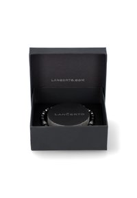 Czarna szkatułka na biżuterię z okrągłym wewnętrznym piedestalem, na którym wyeksponowana jest bransoletka z koralików. Bransoletka ozdobiona jest błyszczącymi czarnymi koralikami i srebrnymi akcentami.