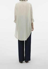 Blusa a righe chiare con orlo arrotondato, maniche a tre quarti e fascette per arrotolare, abbinata a jeans a gamba larga scuri. Tessuto morbido.