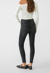 Svart högmidjad skinny jeans i denim, med bakfickor och en åtsittande design. Bärs med en vit off-shoulder topp och svarta ballerina skor.