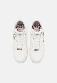 Des sneakers blanches en cuir texturé et en maille, avec un design à lacets, une semelle en caoutchouc, un logo Looney Tunes sur la languette et des semelles intérieures à motifs colorés.