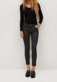 Top negro de manga larga con textura acanalada combinado con jeans gris de corte slim. Los jeans tienen una textura suave, son de tiro alto y cuentan con bolsillos frontales. Mocasines negros completan el conjunto.