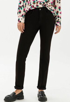 Schwarze Denim-Jeans im Slim Fit mit aufgerollten Säumen, mit einem Knopfverschluss und Fronttaschen, kombiniert mit schwarzen Slippern.