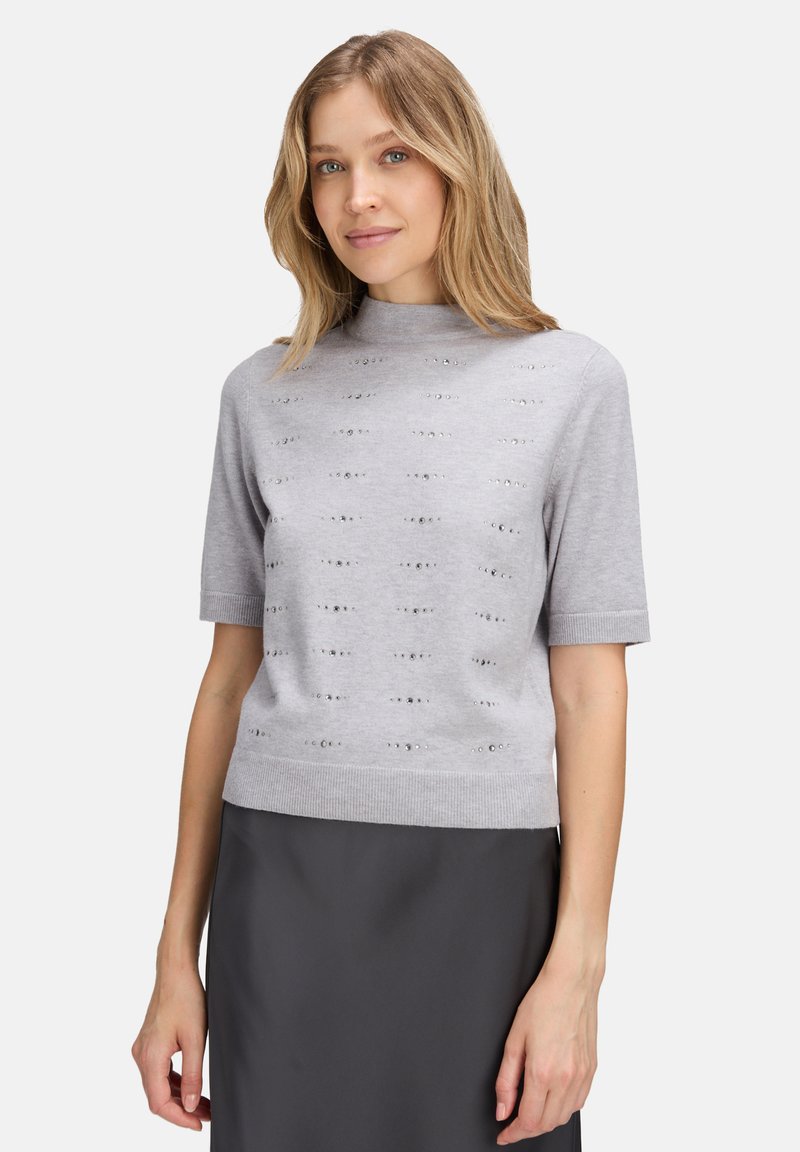 Jasnoszary sweter z krótkim rękawem i wysokim kołnierzem, zdobiony fakturowanym wzorem oraz metalicznymi akcentami. Miękka dzianina; dopasowany krój.