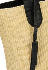 Sac en paille avec un corps beige naturel texturé, des accents en cuir noir et une étiquette avec un logo en relief.
