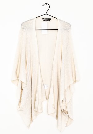 Cárdigan de punto color crema, abierto en el frente y con mangas anchas, colgado en una percha negra sobre fondo blanco.