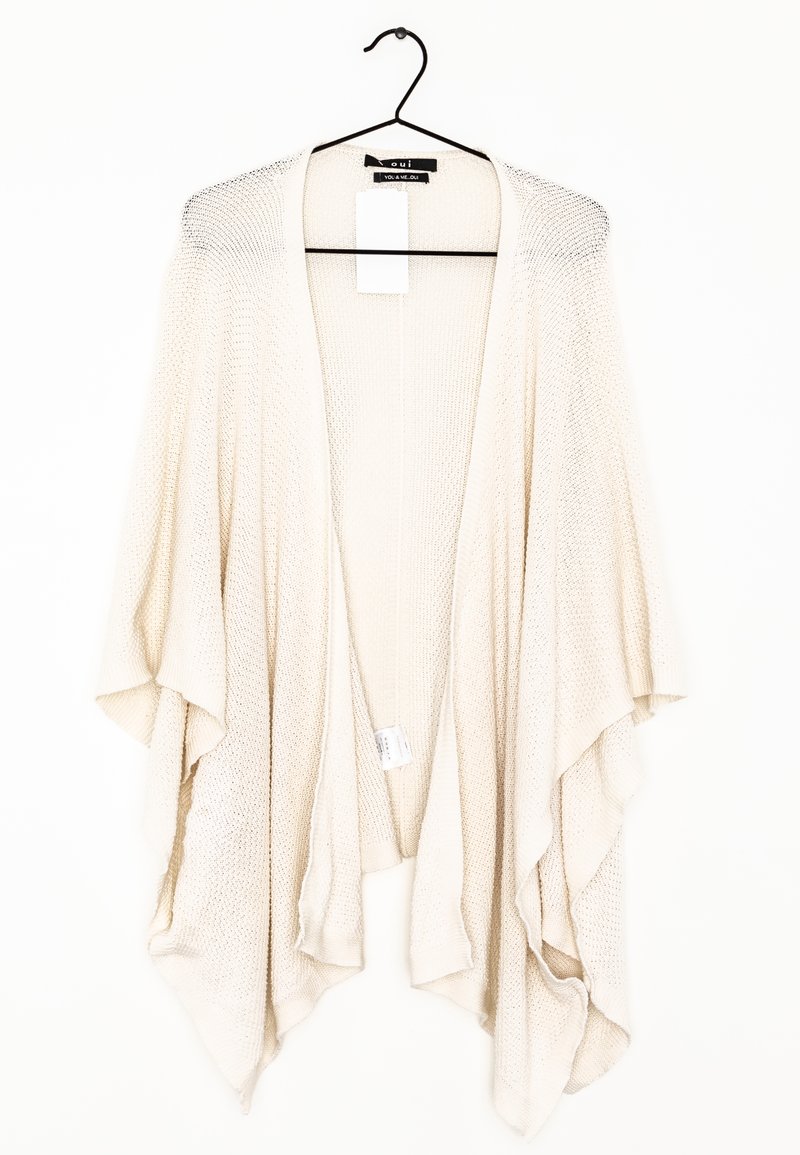 Cardigan tricoté couleur crème à l'avant ouvert avec des manches larges, suspendu à un cintre noir sur fond blanc.