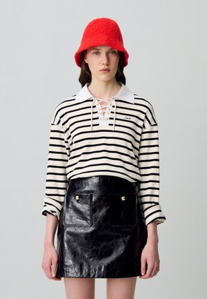 Camisa de manga larga a rayas en crema y negro con cuello con cordones; minifalda de cuero ecológico negro brillante con dos bolsillos frontales y botones dorados. Sombrero de cubo de lana roja.