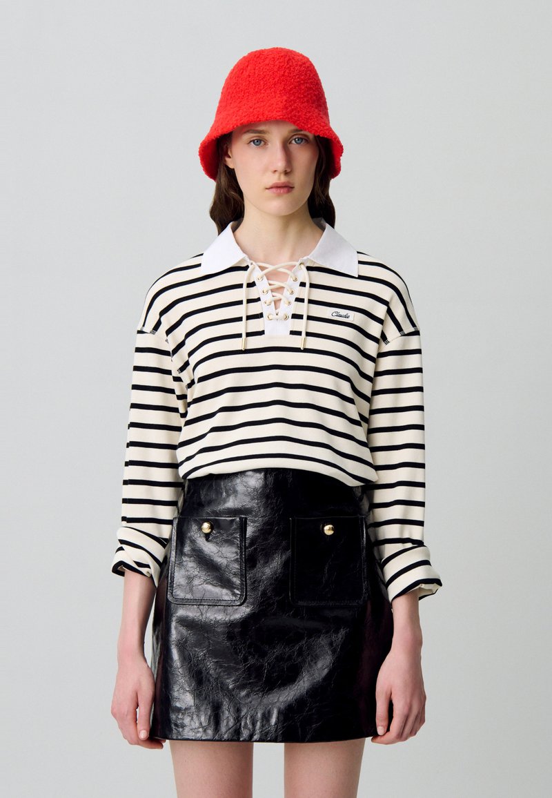 Camisa de manga larga a rayas en crema y negro con cuello con cordones; minifalda de cuero ecológico negro brillante con dos bolsillos frontales y botones dorados. Sombrero de cubo de lana roja.