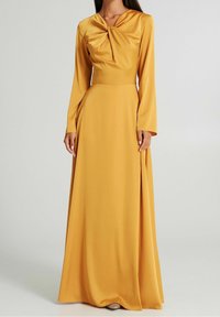 Senapsgul långärmad klänning med knytkrage, flödande kjol och slits på sidan, tillverkad av ett glatt tyg. Har en figursydd överdel.