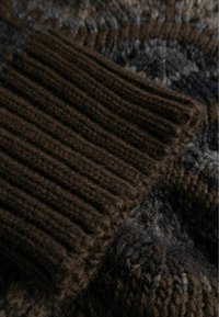 Rudas megztas džemperis, turintis rauktus rankogalius, tekstūruotus pilkus raštus ir minkštą išvaizdą su skirtingais siūlo storio lygiais.