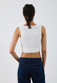 Top scurt alb din bumbac cu textură côtée, asortat cu blugi negri cu talie înaltă, având două buzunare în spate și cusături contrastante.