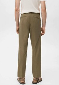 Pantalones verde oliva de corte recto, con dos bolsillos en la parte trasera y detalles de costura sutiles. Se llevan con una blusa de color claro y sandalias.