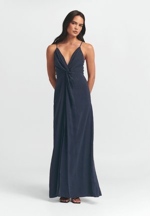 Marineblauwe maxi-jurk met een diepe V-hals en geknoopte voorkant. Gemaakt van lichtgewicht stof, met dunne bandjes en een vloeiende silhouette.