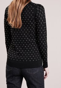 Czarny sweter dzianinowy z wzorem w diamenty ozdobionymi metalicznymi koralikami. Długie rękawy i prążkowane mankiety dopełniają design.