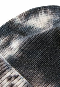 Strickmütze in einem melierten Grau- und Weißton. Die Textur ist weich und besitzt gerippte Details am Rand.