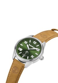 Reloj con esfera verde, caja de acero inoxidable plateada, marcadores horarios blancos, pequeño sub-dial y correa de cuero marrón. Logo de Timberland grabado en la correa.