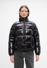 Melna pūkainā virsjakas ar augstu apkakli, spīdīgu apdari, horizontālu kvadrātu rakstu, priekšējo rāvējslēdzēja aizdari un elastīgām aprocēm un apakšmalu.