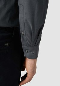 Dunkelgraues Langarmshirt mit geknöpften Manschetten, einer glatten Textur und Stichdetails. Nahaufnahme des Arms und der Manschettenbeschläge des Shirts.